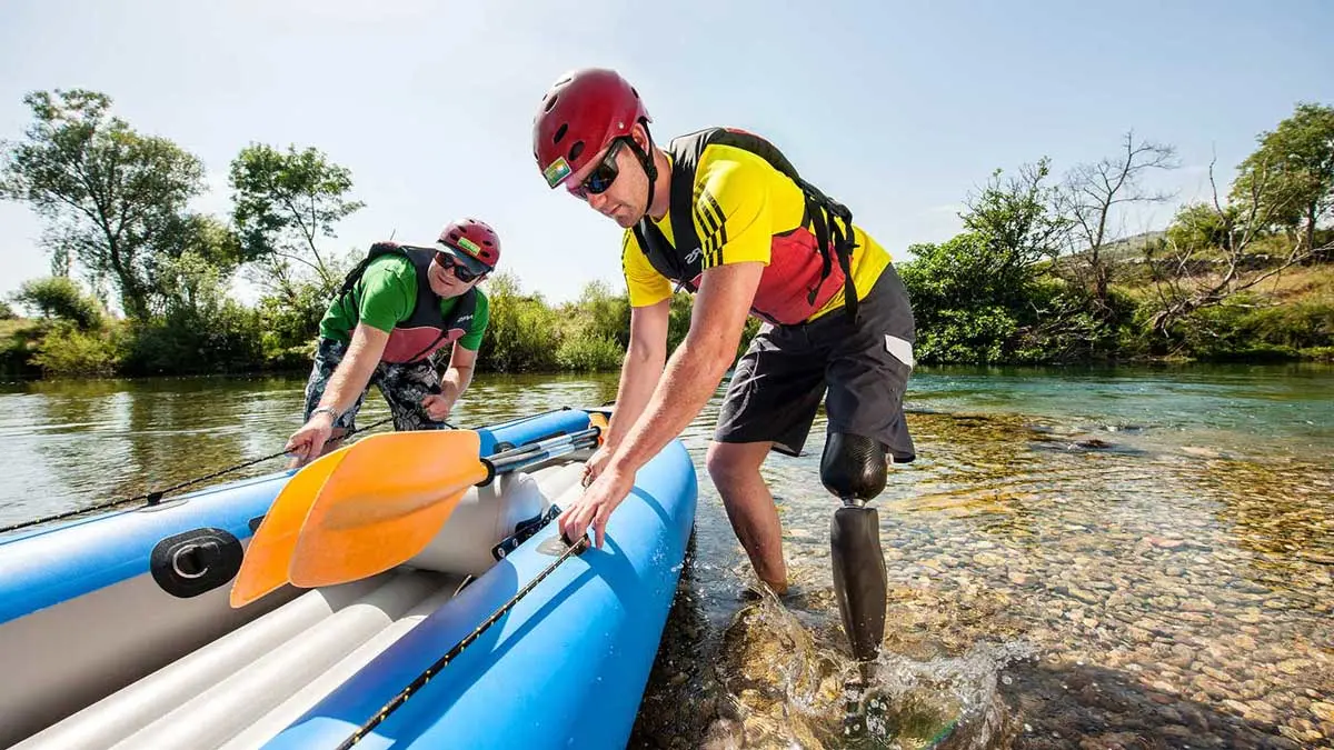 A prosthetic knee user standing in a body of water preparing a water raft 
