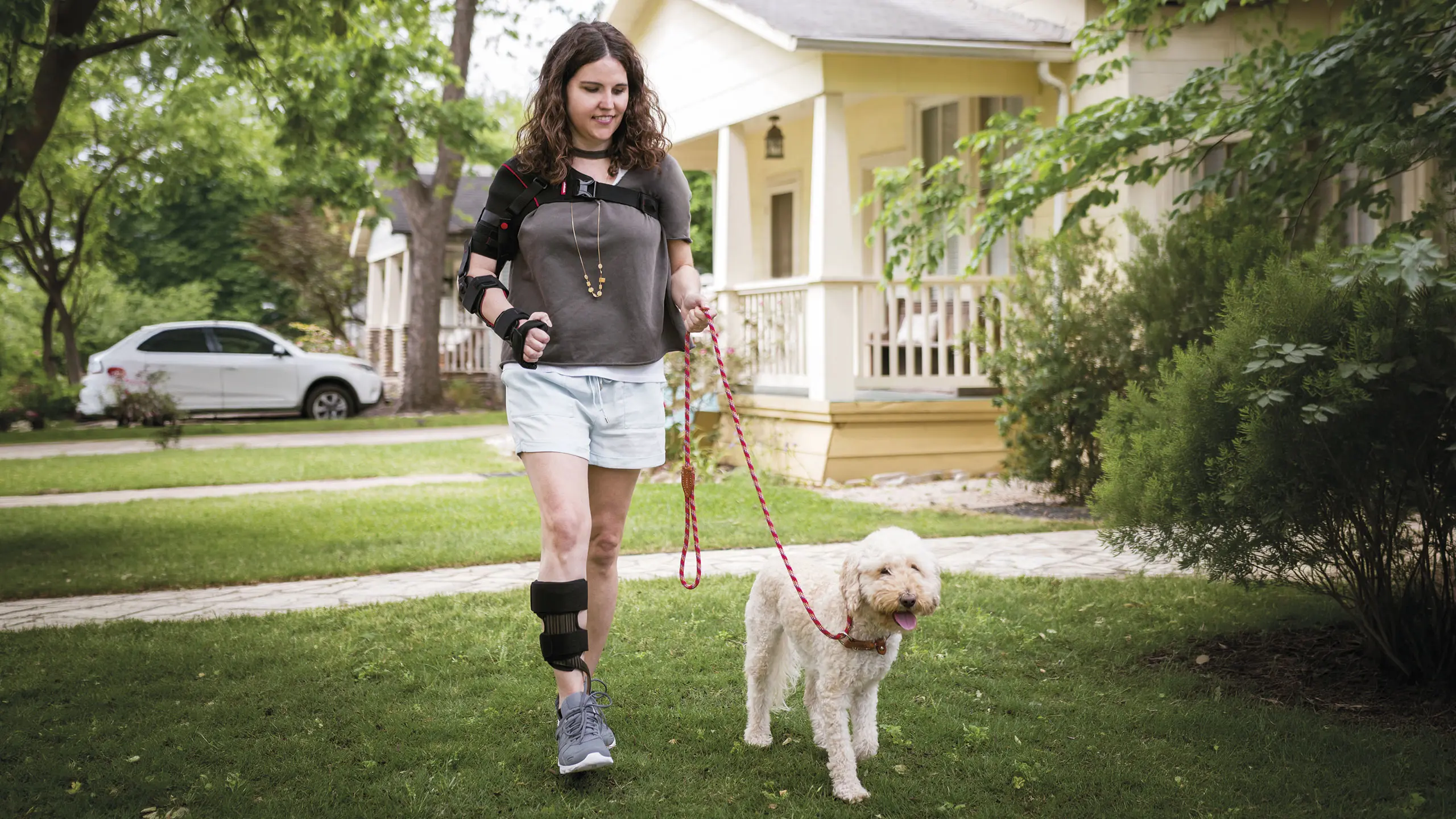 Una ragazza porta a spasso il cane al guinzaglio mentre indossa l'ortesi di polso Manu Neurexa Plus combinata all'ortesi di spalla Omo Neurexa Plus