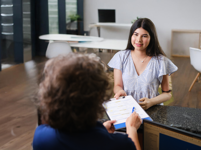 Un administrador de recepción entregando a un paciente con un brazo protésico el papeleo para completar antes de su cita