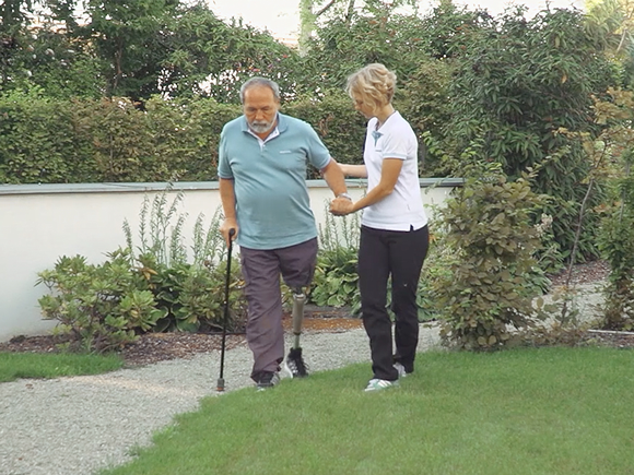 Una persona mayor caminando por un césped al aire libre con su prótesis de pierna con la ayuda de un ortopedista certificado 