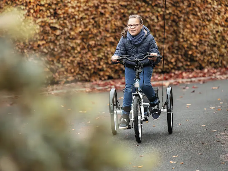Una bambina guida il suo triciclo Momo al parco in autunno