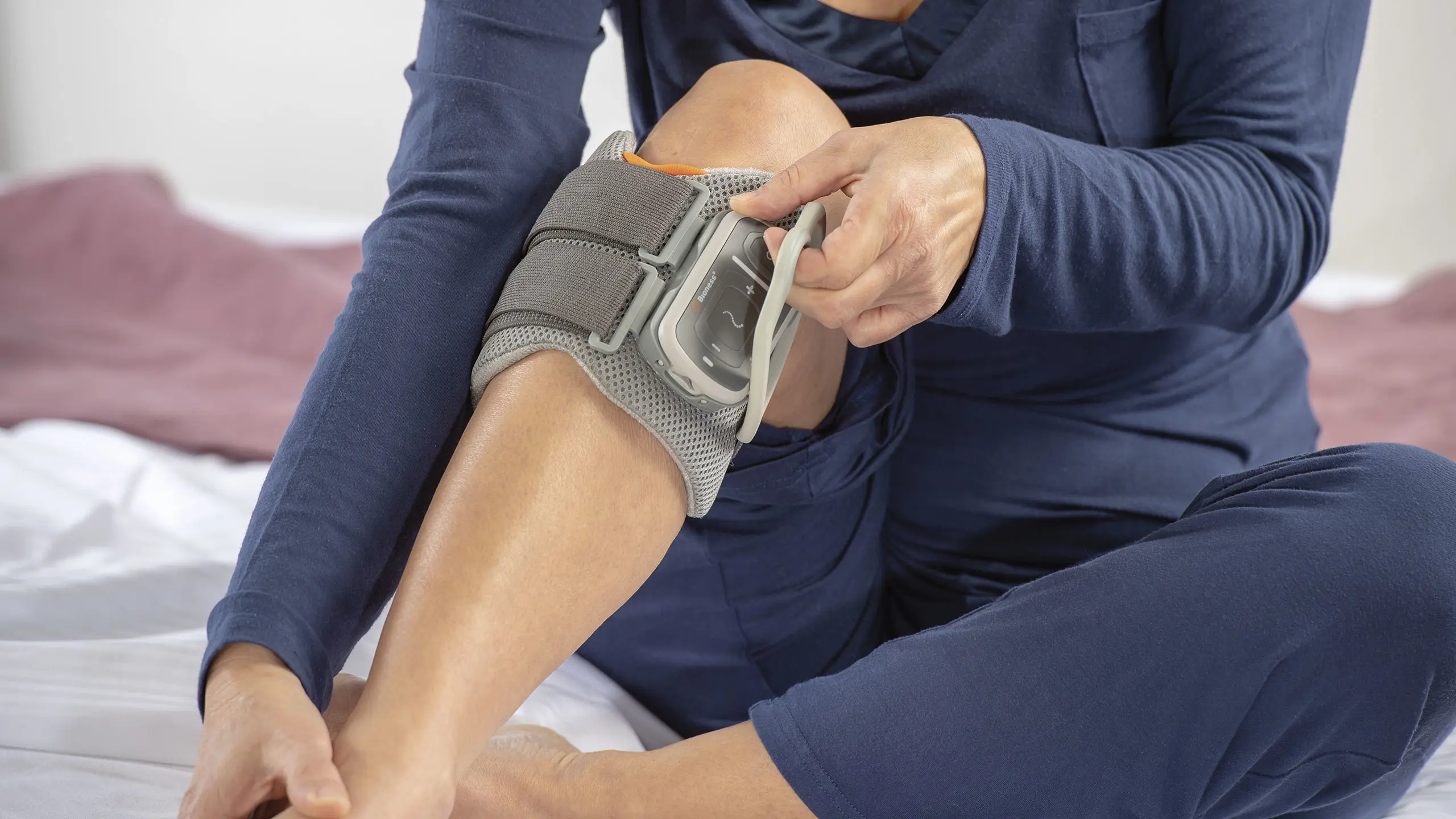 Dettaglio di una paziente seduta sul letto che con una sola mano indossa L300 Go