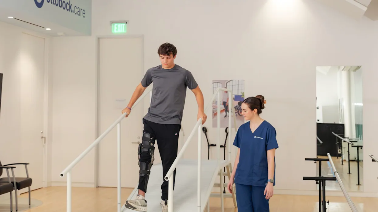 A limb difference patient testing the C-Brace knee ankle foot orthosis while walking down an incline in a clinical setting, guided by their Certified Prosthetist Orthotist