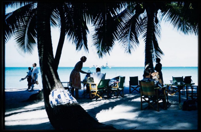 TEAL passengers having breakfast at Akaiami, Aitutaki, Cook Islands. A TEAL Solent is moored in the background. Hajo Topzand. 1950s. PHO-2004–3510.28. Walsh Memorial Library, Museum of Transport and Technology (MOTAT)