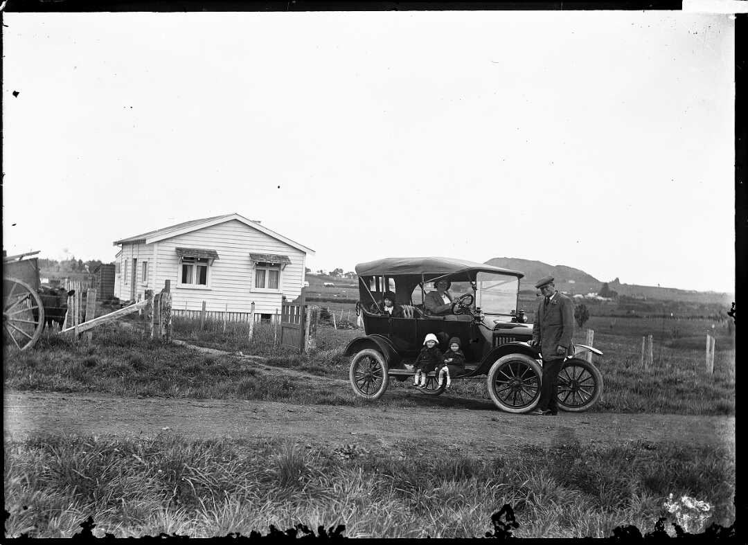 A vintage Ford Model A car in front of a colonial house in