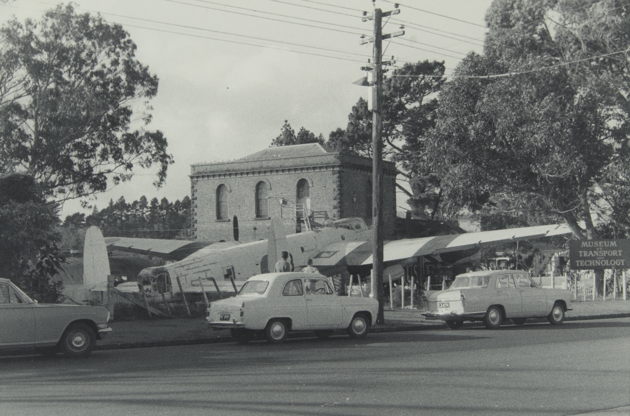 Pumphouse and aircraft at MOTAT Great North Road site. Photographed by Murray Johnston, late 1960s, PHO-2020-1.18. Walsh Memorial Library, The Museum of Transport and Technology (MOTAT).