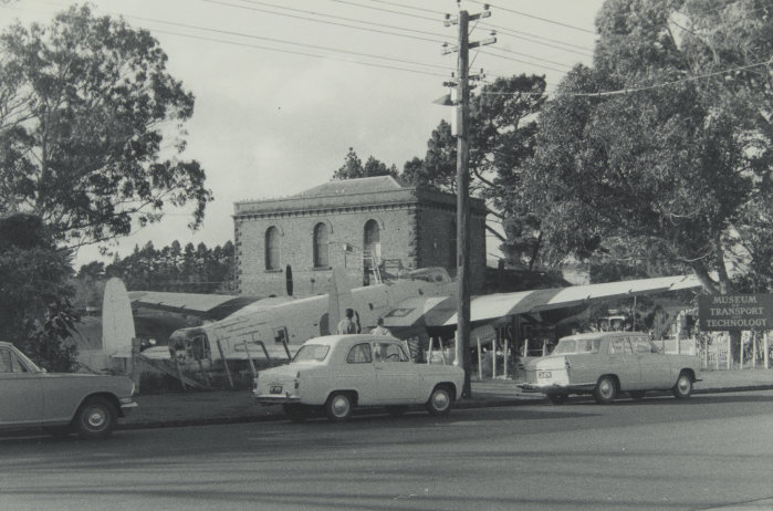 Pumphouse and aircraft at MOTAT Great North Road site. Photographed by Murray Johnston, late 1960s, PHO-2020-1.18. Walsh Memorial Library, The Museum of Transport and Technology (MOTAT).