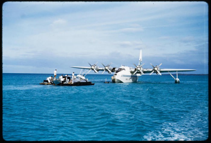 Refuelling barge towed out to Solent at Aitutaki, Cook Islands. The Solent was refuelled by local labour hand pumping fuel from drums with flight and ground engineers supervising. Hajo Topzand, 1950s. PHO-2004–3510.29. Walsh Memorial Library, Museum of Transport and Technology (MOTAT)