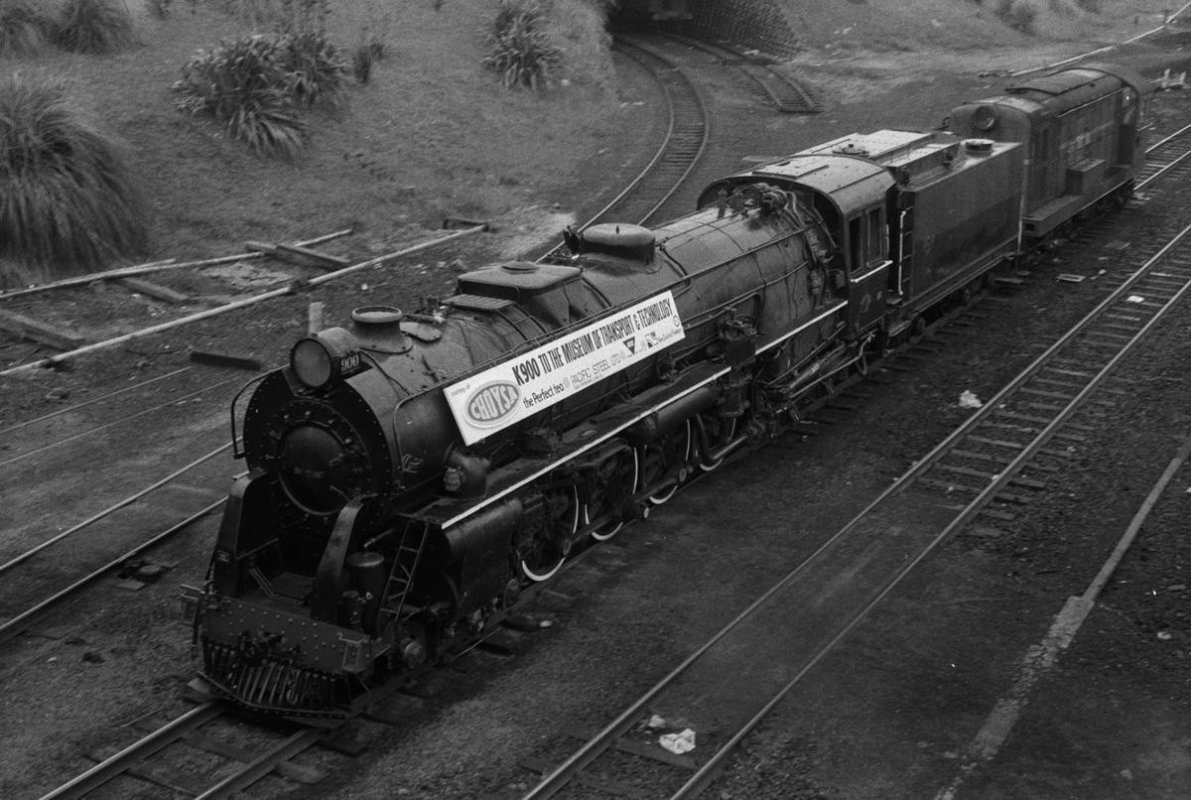 K900 locomotive being towed to MOTAT by diesel engine: CHOYSA tea banner attached. Les Downey. 1972–1976. Photograph of locomotive K 900, 14–1369