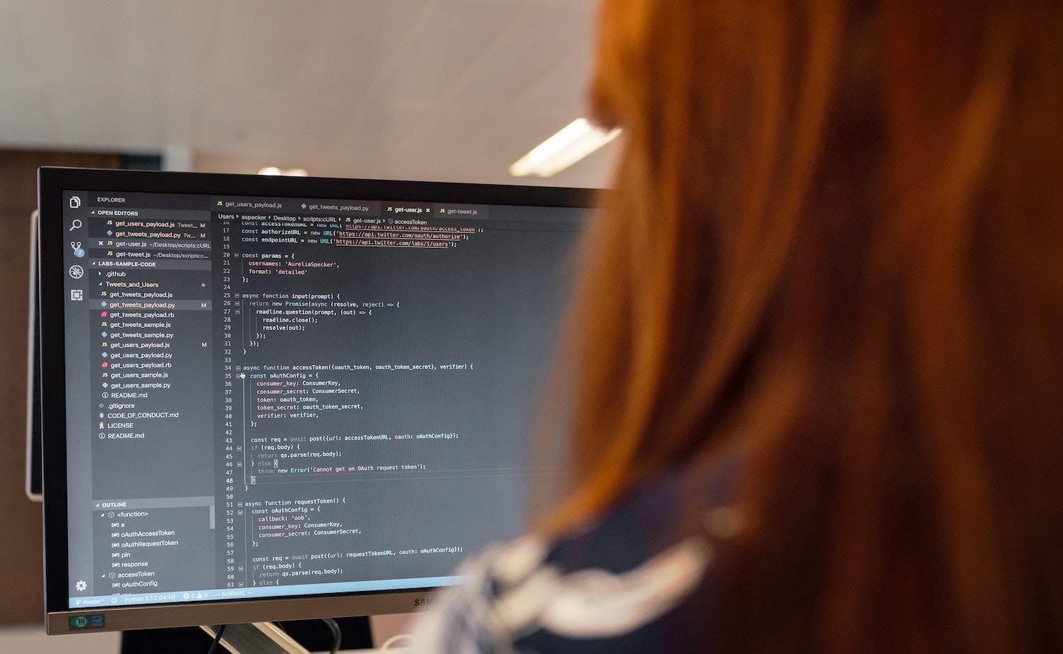 Woman working on a computer. She has red, long hair, and coding editor open in her external screen. 