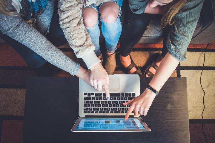 Top down view of multiple persons pointing at the screen of a macbook