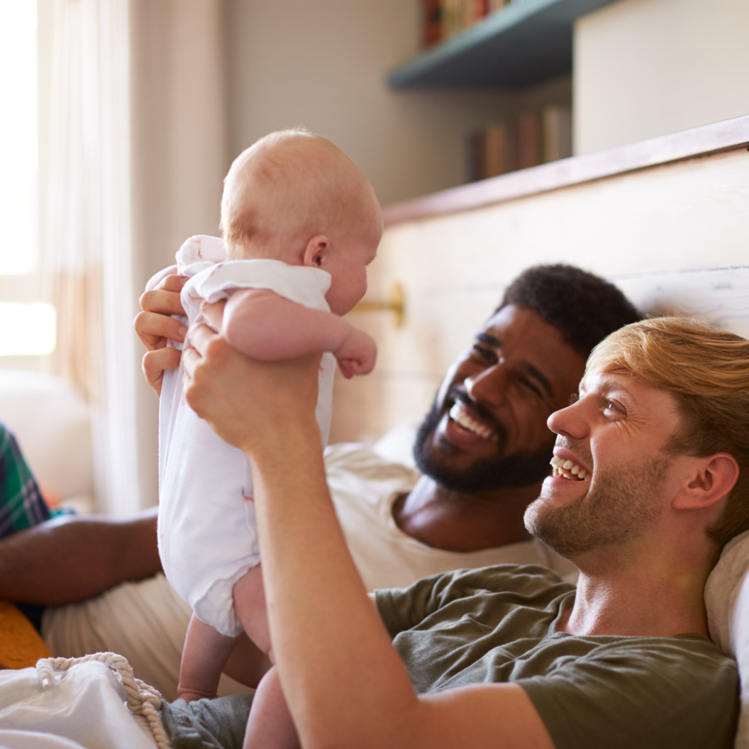 square-loving-male-same-sex-couple-cuddling-baby-daughter-in-bedroom-at-home-together