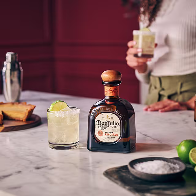 Two glasses of Reposado Margarita in the foreground with a bottle of Don Julio Reposado in the background alongside five candles