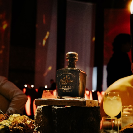 A bottle of Don Julio tequila is prominently displayed on a stone pedestal in a dimly lit, elegant setting.