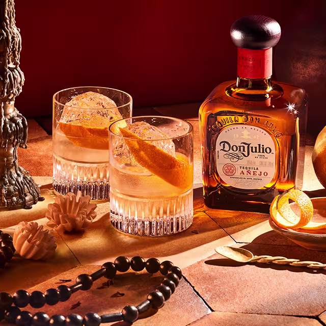 A glass filled with an Old Fashioned cocktail on a table next to a bottle of Don Julio Añejo