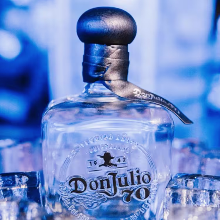 A bottle of Don Julio 70 tequila is centered among several shot glasses.