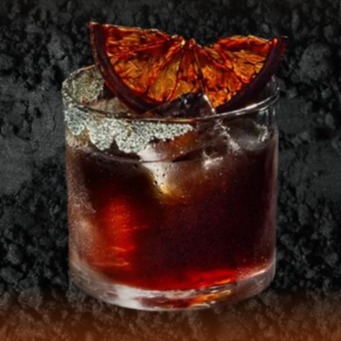 Image of a cocktail served in a short glass with a dark, rich liquid and ice cubes. The rim of the glass is coated with sugar crystals, adding texture and sparkle.