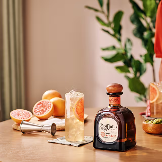 A bottle of Don Julio Reposado on a table in between two glasses filled with Don Julio Paloma cocktail recipe
