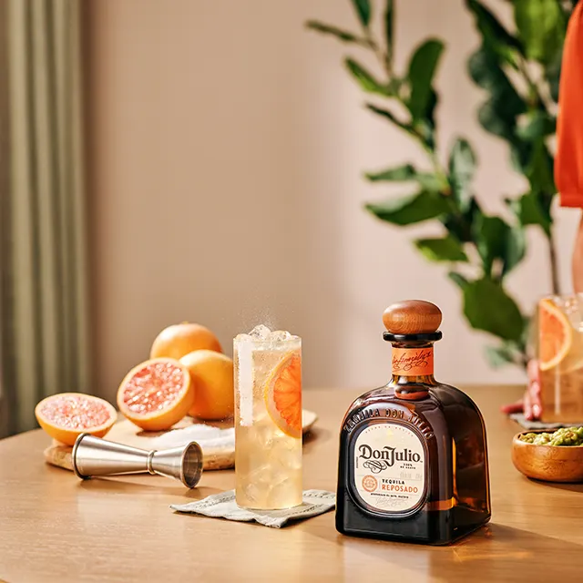 A bottle of Don Julio Reposado on a table in between two glasses filled with Don Julio Paloma cocktail recipe