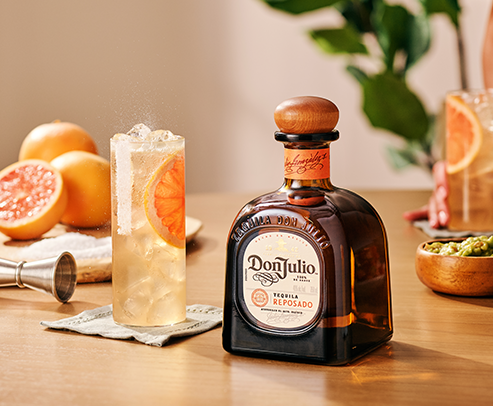 A bottle of Don Julio Reposado on a table in between two glasses filled with Don Julio Paloma cocktail recipe