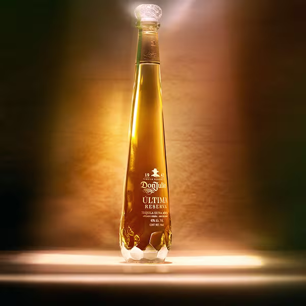 A bottle of Don Julio Ultima Reserve on a table in a dark room with a beam of light illuminating the bottle from above