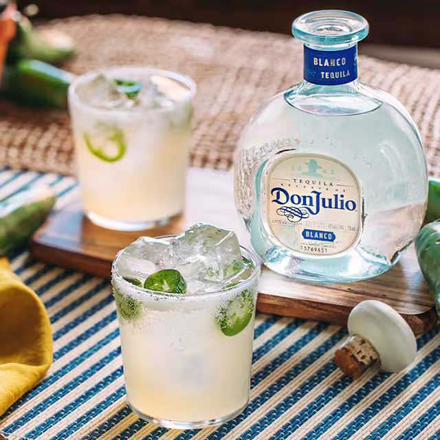 Two glasses of Blanco Spicy Margarita cocktail being help by two people having a conversation