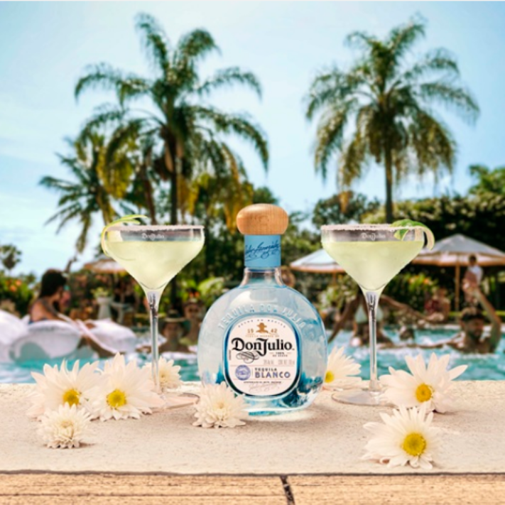 A bottle of Don Julio Blanco tequila is elegantly placed between two margarita glasses garnished with lime slices.