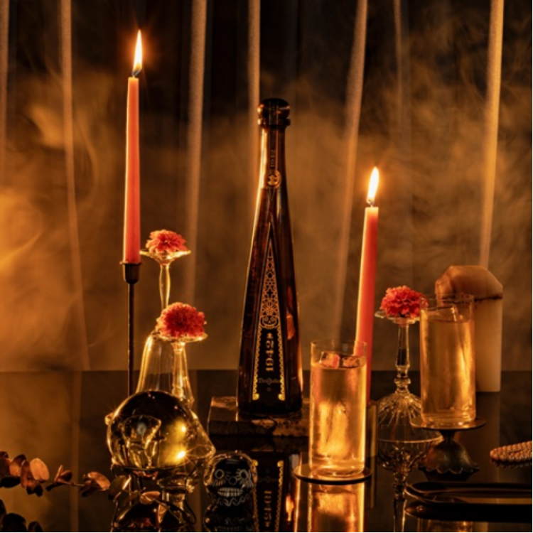 A dramatic and elegant scene featuring a tall, dark bottle of liquor surrounded by glowing candles and delicate floral arrangements.
