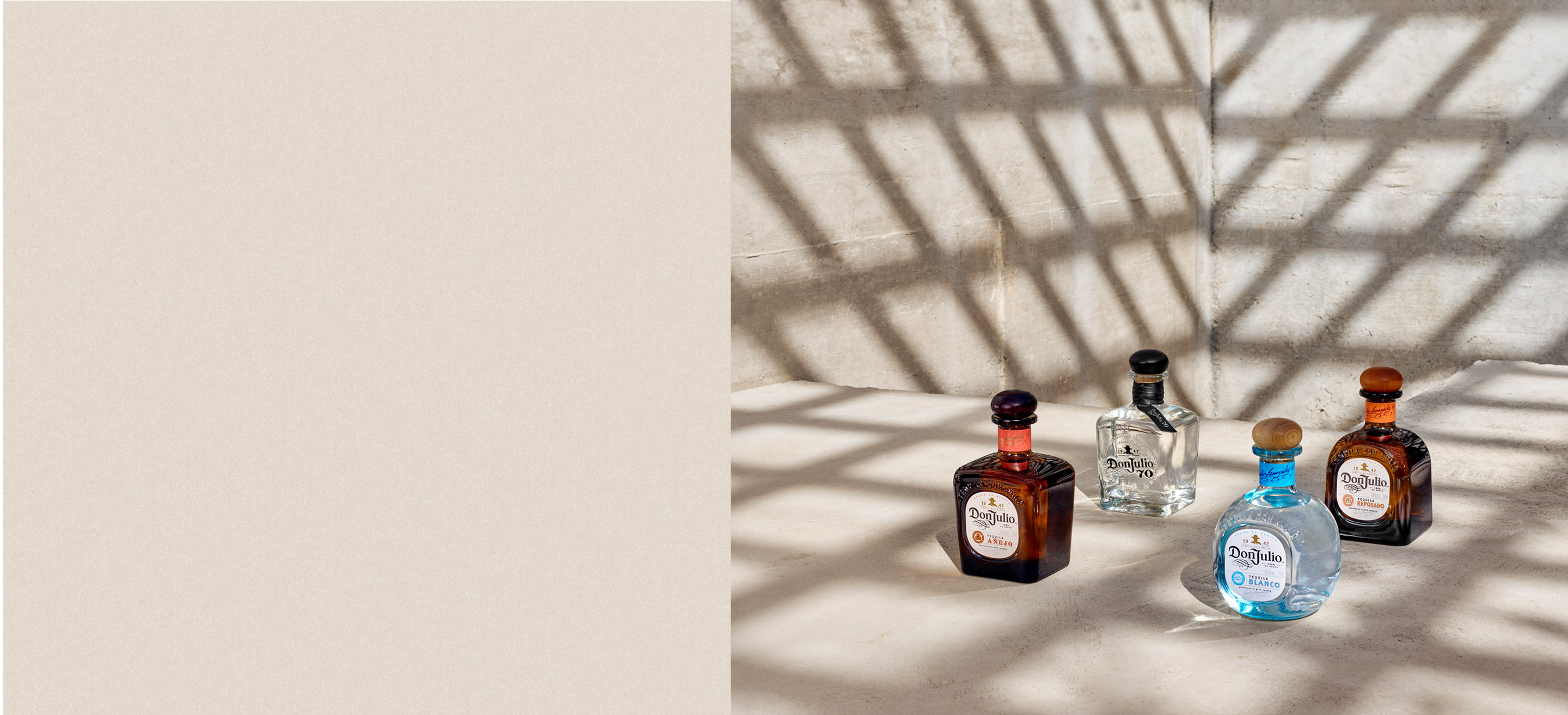 A bottle of Don Julio Blanco, Don Julio Añejo, Don Julio Reposado, and Don Julio 70 Cristalino on a table with a lattice shadow around them