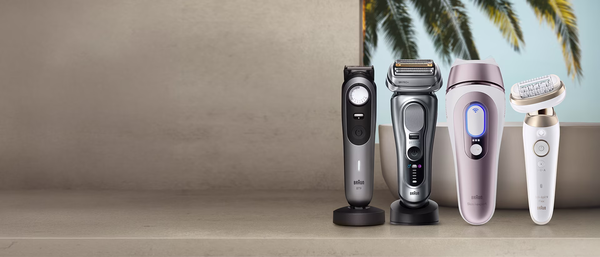 Cuatro dispositivos Braun alineados sobre una superficie beige frente a hojas de palmera: recortadora de barba Braun BT9, afeitadora Braun Series 9 Pro+, dispositivo IPL Braun Skin i·expert y depiladora Braun Silk·épil 9 Flex.