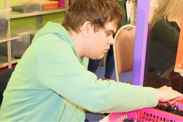 A Loddon Social Enterprise service user working. They are wearing a green hoodie whilst sat picking items out of a red plastic container.