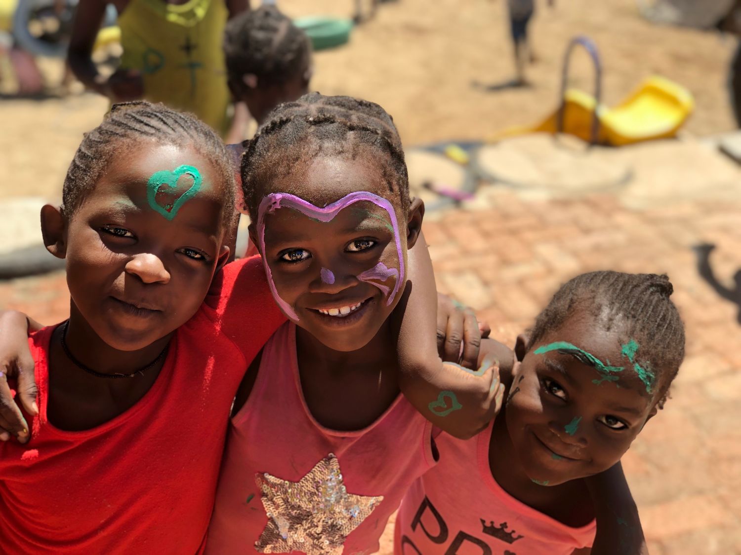 Drei namibianische Freundinnen mit Farbe von Streichen einer Schule im Gesicht lachen in die Kamera. 