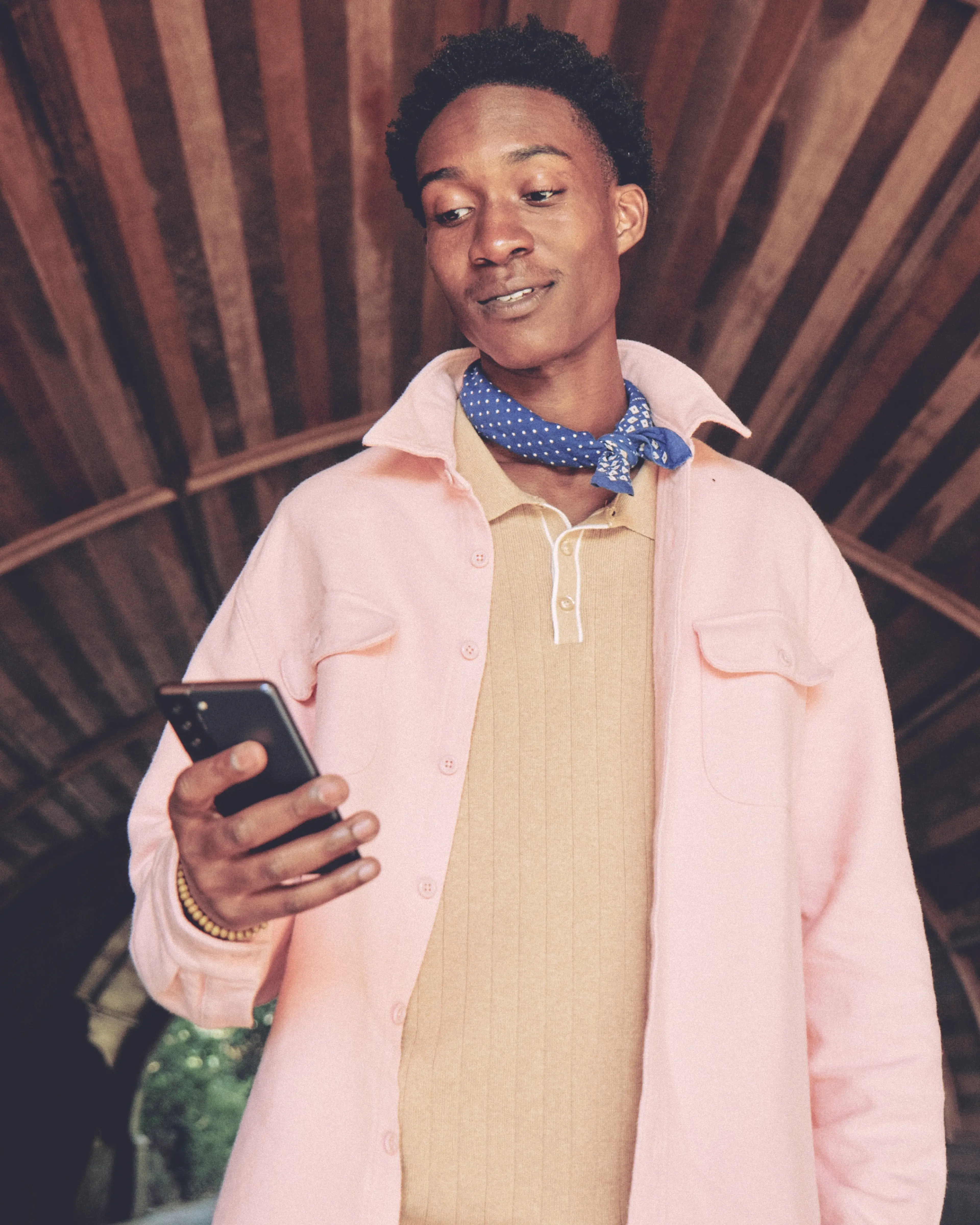 A stylish man smiling and looking down at his smart phone.