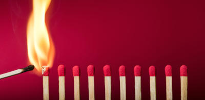 A burning match stick setting fire to a row of unlit match sticks