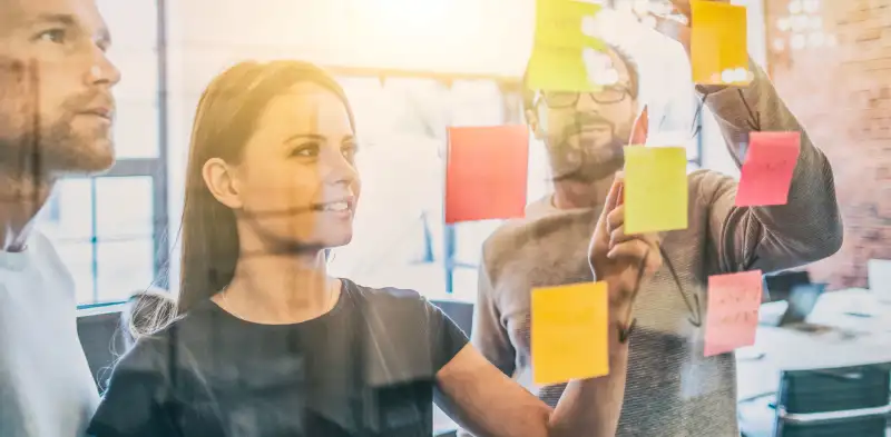 woman sticking post-it notes to glass wall, whiteboard okrs, okrs on post-it notes, okrs on sticky notes