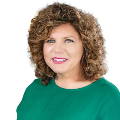  woman with curly brown hair and blue eyes smiles at the camera. She is wearing a vibrant green top and is pictured against a transparent background. 
