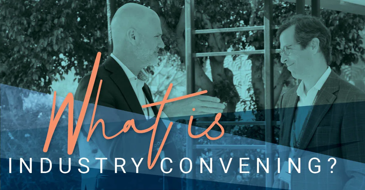 Two professionals in conversation under a shaded outdoor setting, overlaid with stylized text asking, “What is Industry Convening?” in large script and block letters.