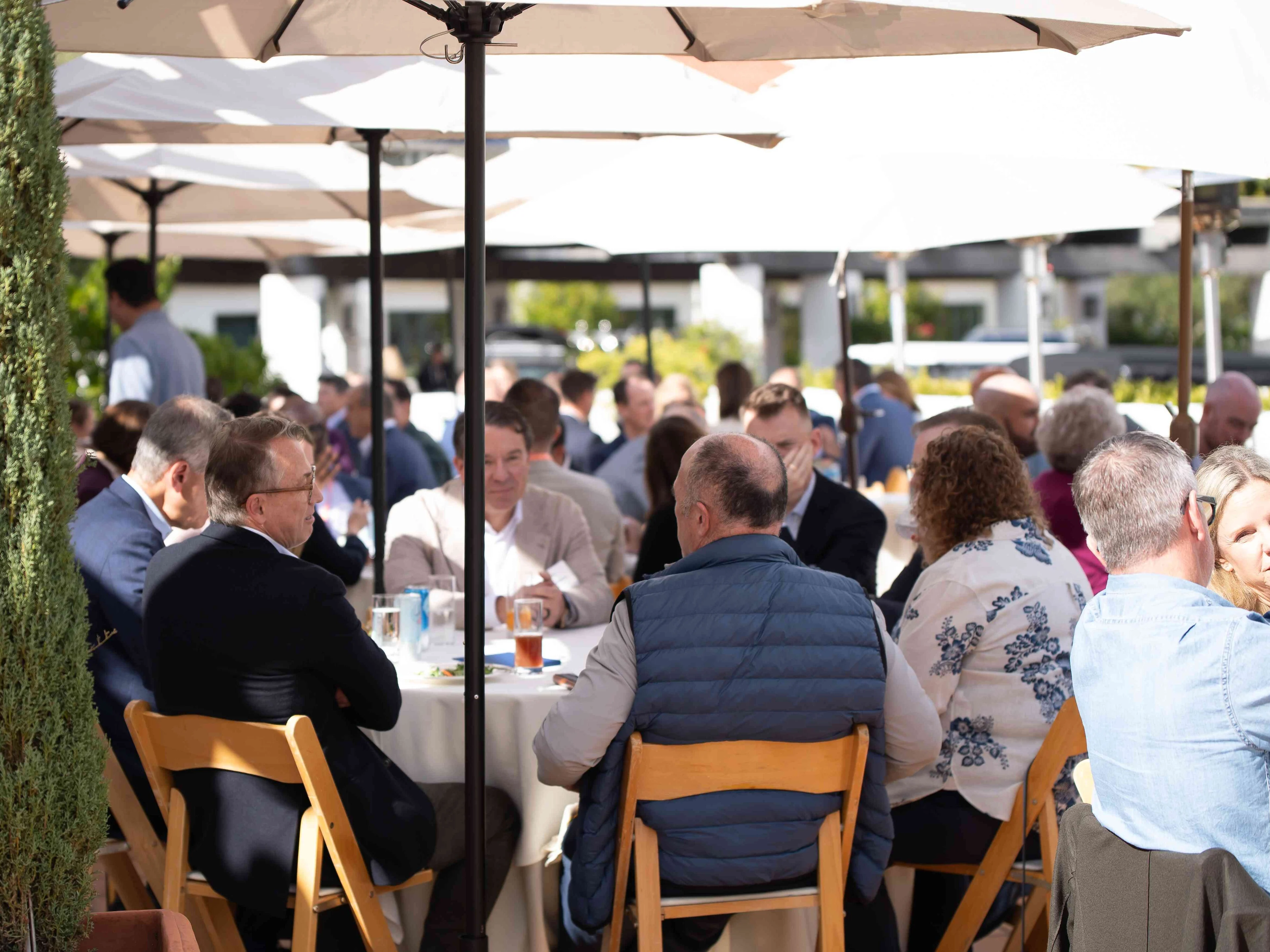 Attendees gather outdoors for networking conversations during healthcare medical conferences, seated at round tables under umbrellas.