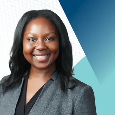A woman wearing a gray blazer and black blouse smiling in front of a geometric blue and teal background.