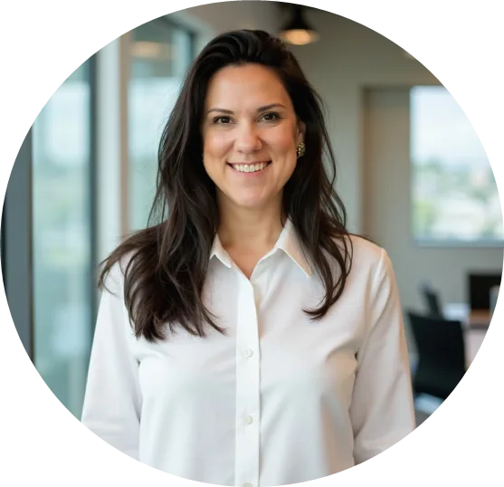 Woman in a white blouse smiling for a headshot in a modern office with large windows and blurred background.