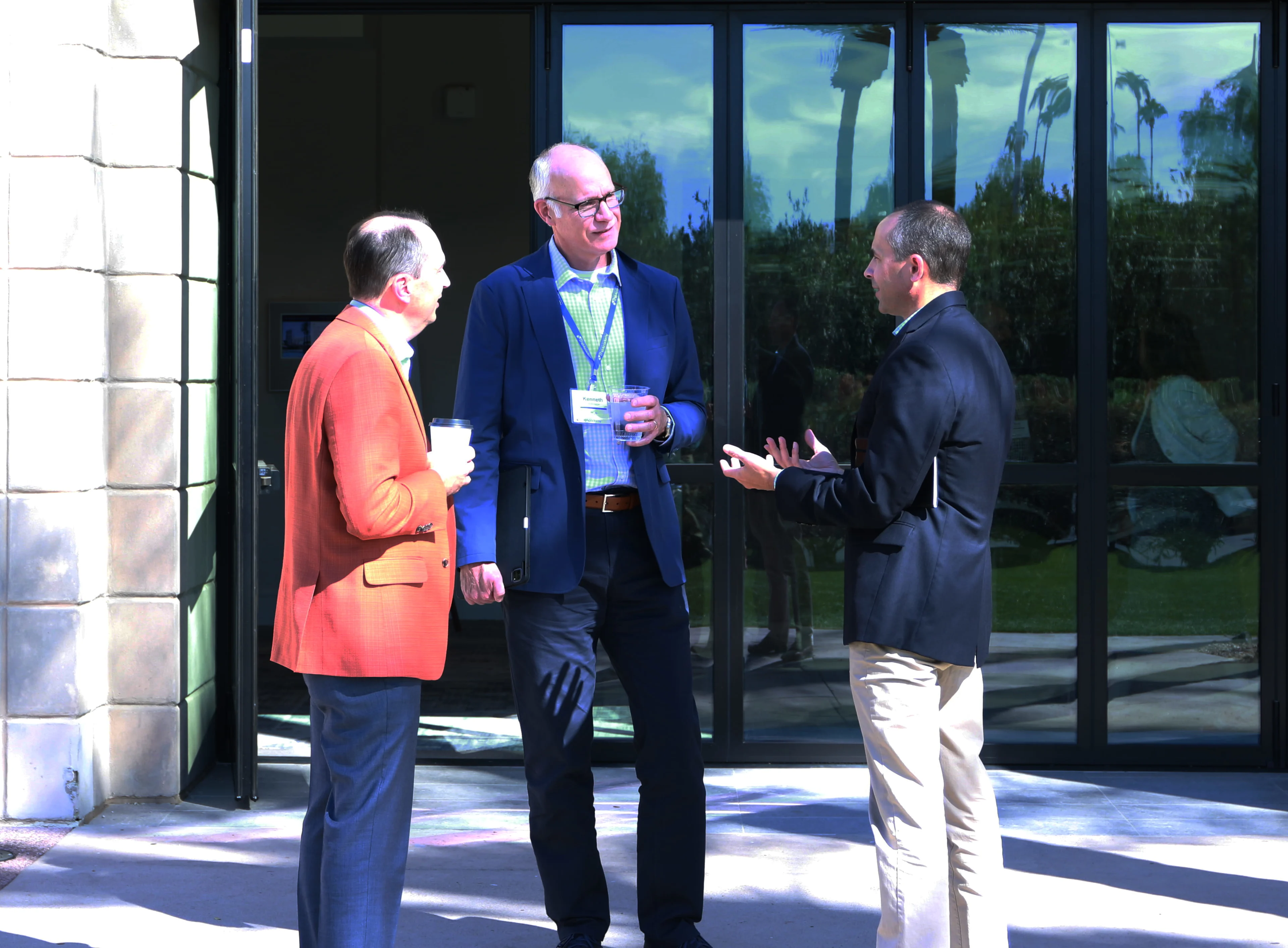Three professionals in business casual attire speaking outside a venue during a conference networking session.