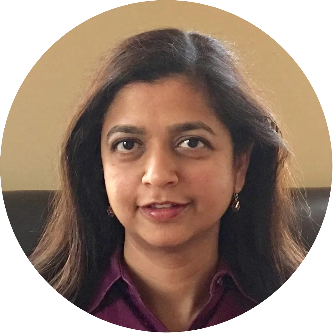 Woman with long dark hair wearing a maroon blouse, posing for a headshot indoors against a neutral beige background. She is looking directly at the camera with a subtle smile.