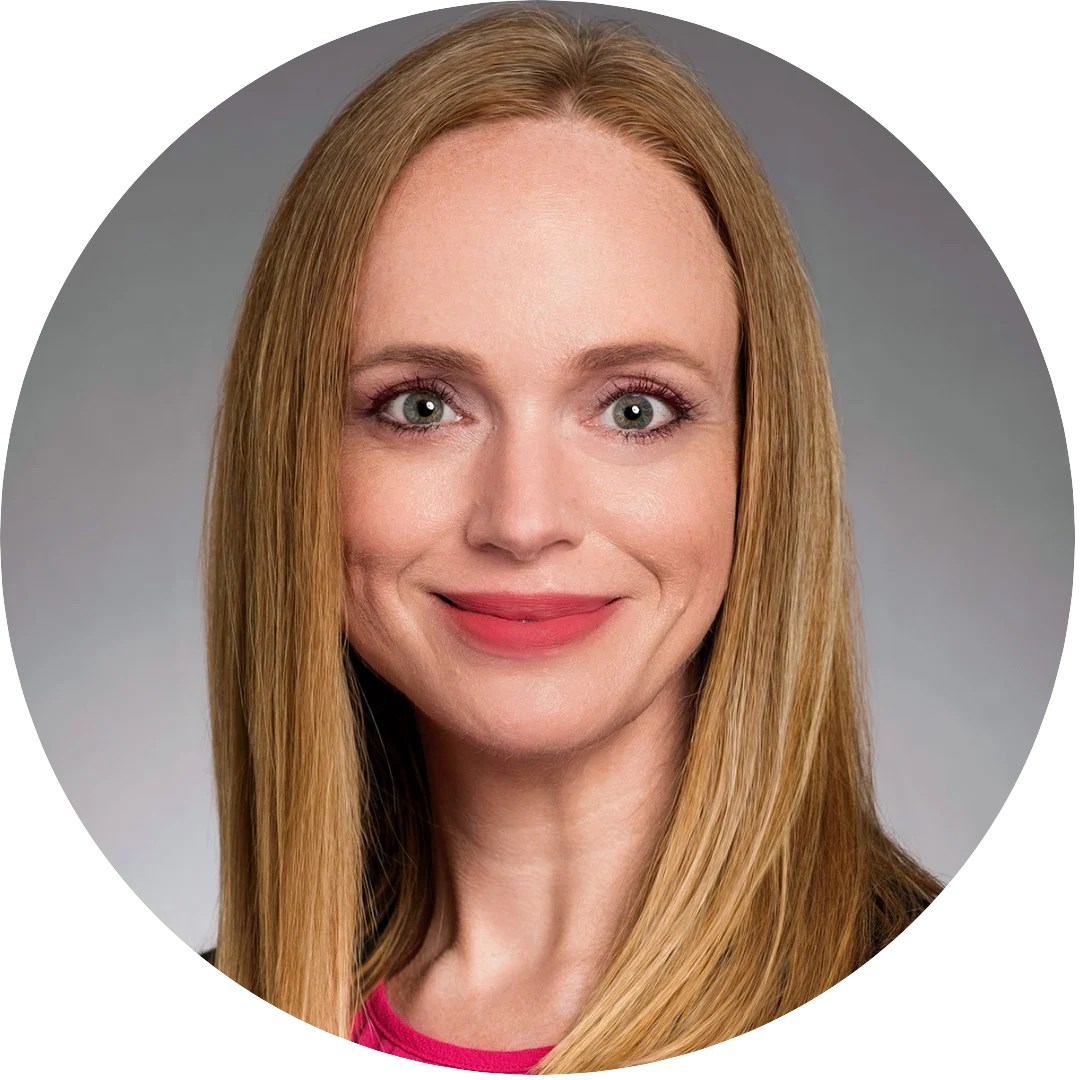 Smiling woman with long straight blonde hair wearing a bright pink top, posed against a neutral gray background for a formal headshot.
