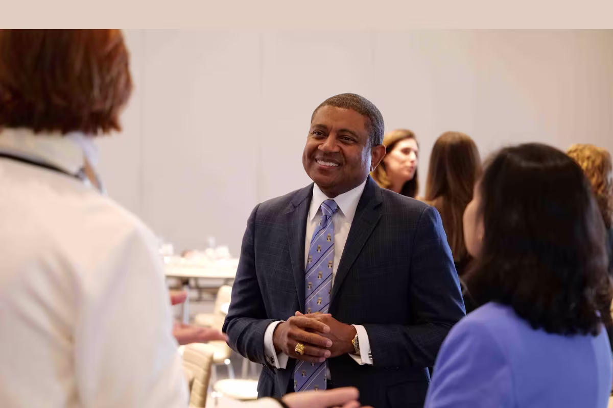 A man in a suit smiling and talking with two women at a professional networking event.