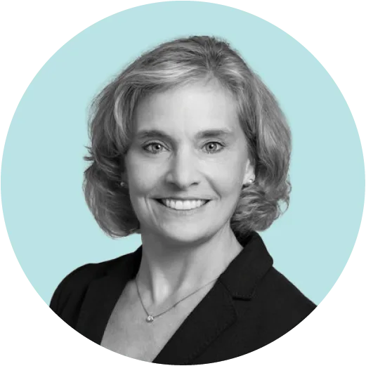 Black and white portrait of a smiling woman with shoulder-length wavy hair, wearing a dark blazer and necklace, set against a light teal circular background.