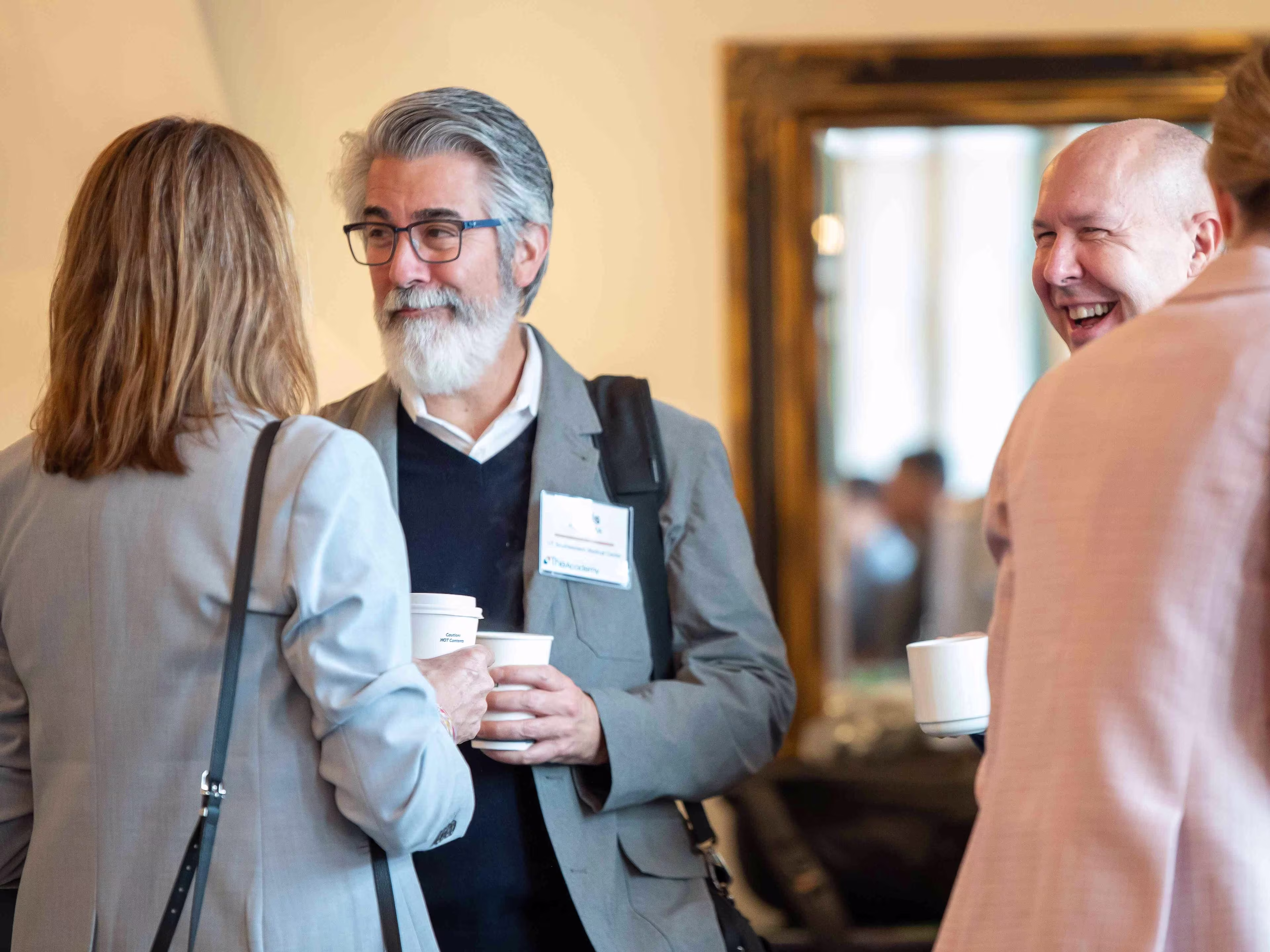 Professionals speak and network over coffee during healthcare operations and administration conferences inside a bright conference venue.