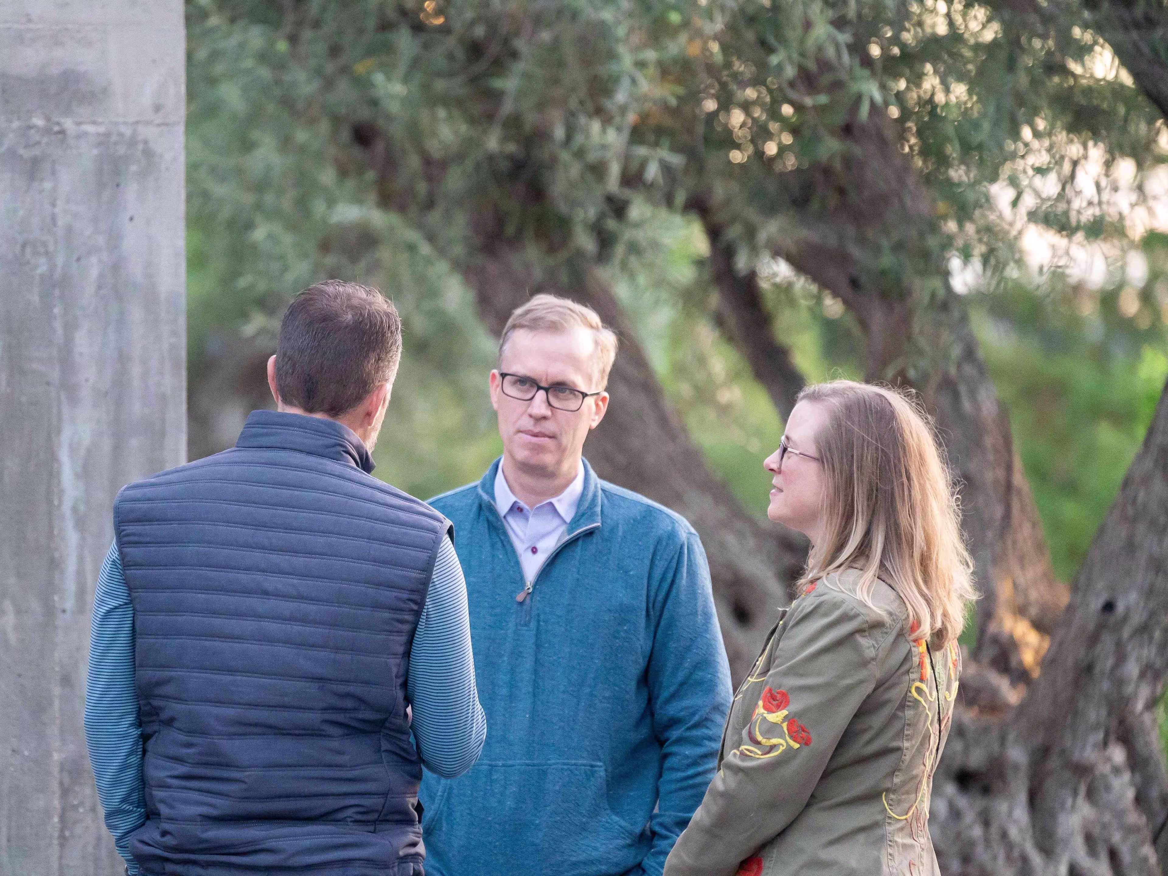 Three professionals networking outdoors during healthcare executive leadership conferences, standing near a modern concrete structure and trees.