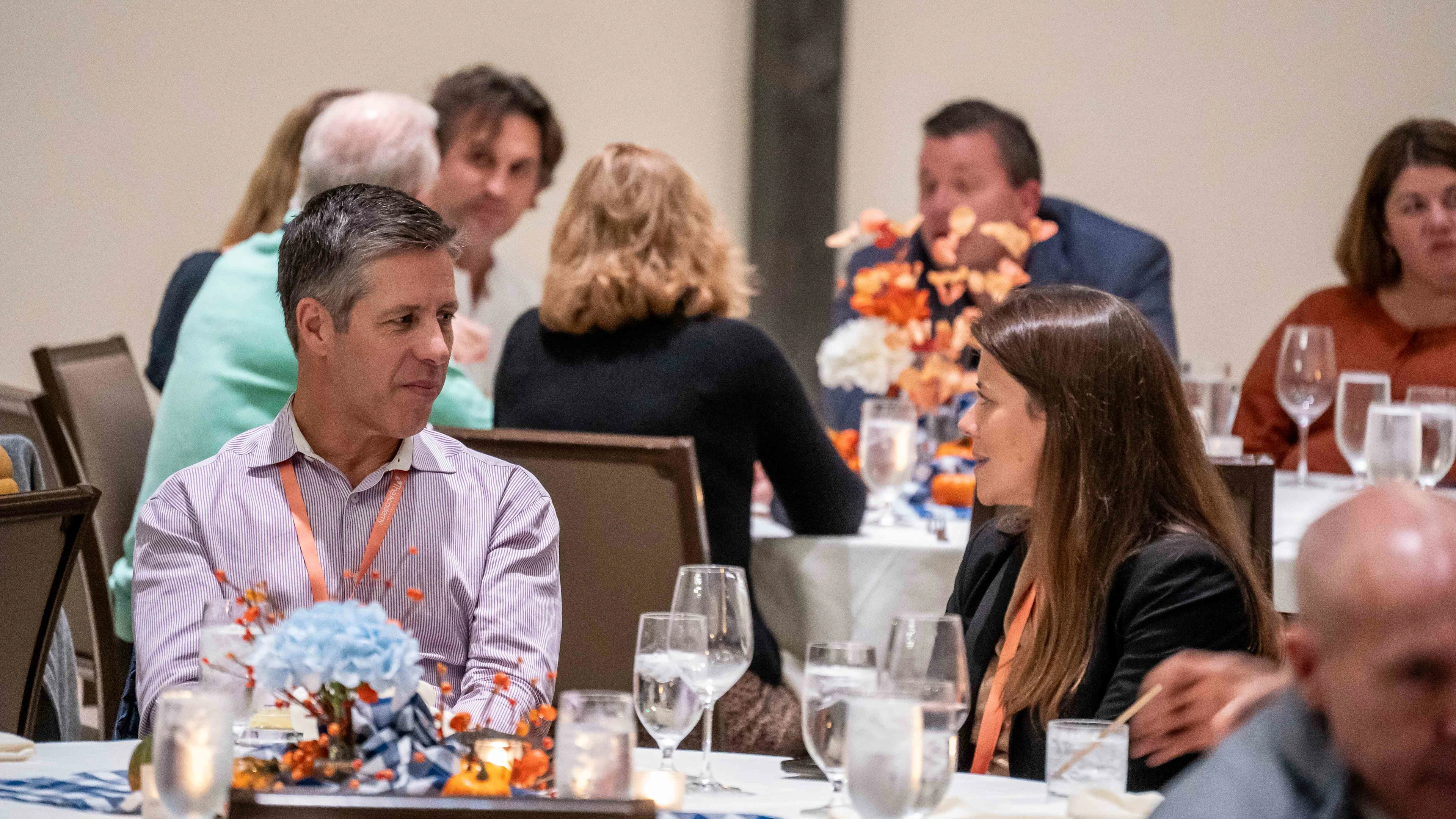 Attendees seated at a round table engaging in conversation during a healthcare financial management conference, with floral centerpieces and glassware set for a formal dinner.
