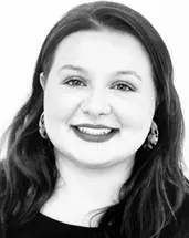 Grayscale image of a woman smiling at the camera, with long dark hair, wearing earrings and a dark top.