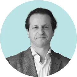 A man in a blazer and white shirt smiling slightly in a professional headshot, set against a light blue circular background.